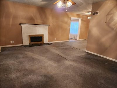 Living room featuring a brick fireplace and a ceiling fan, carpet flooring, and a textured ceiling | Image 3