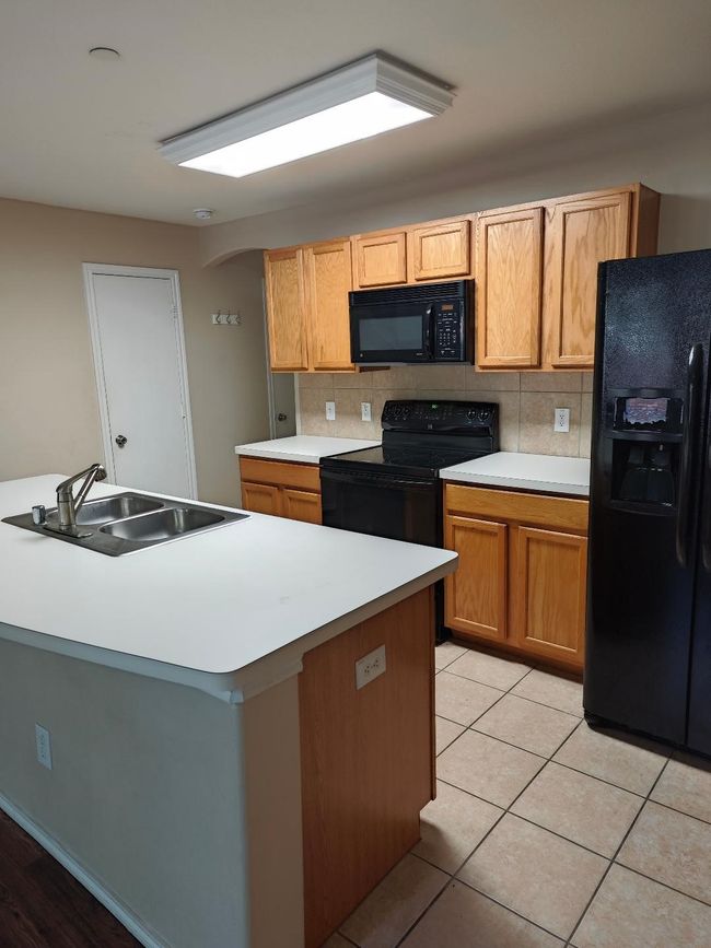 Kitchen with black appliances, a sink, tasteful backsplash, and light countertops | Image 5