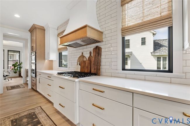 Kitchen featuring light countertops, custom exhaust hood, light wood finished floors, white cabinetry, and tasteful backsplash | Image 16