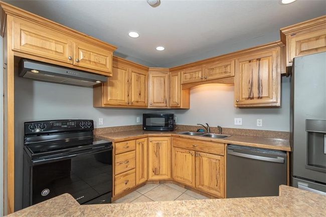Kitchen featuring light tile patterned flooring, recessed lighting, a sink, black appliances, and under cabinet range hood | Image 17
