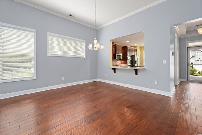 Interior space featuring crown molding, visible vents, baseboards, dark wood-style flooring, and a notable chandelier | Image 13