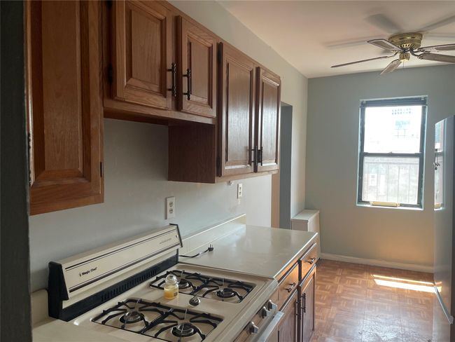 Kitchen with gas range oven, a ceiling fan, light countertops, baseboards, and brown cabinets | Image 9