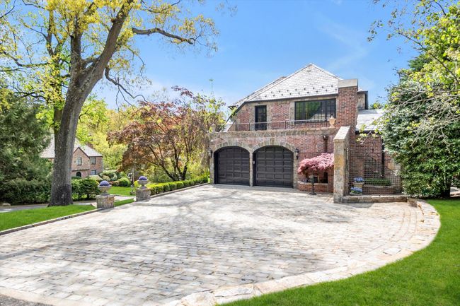 View of front of home with a high end roof, brick siding, decorative driveway, a garage, and a balcony | Image 4