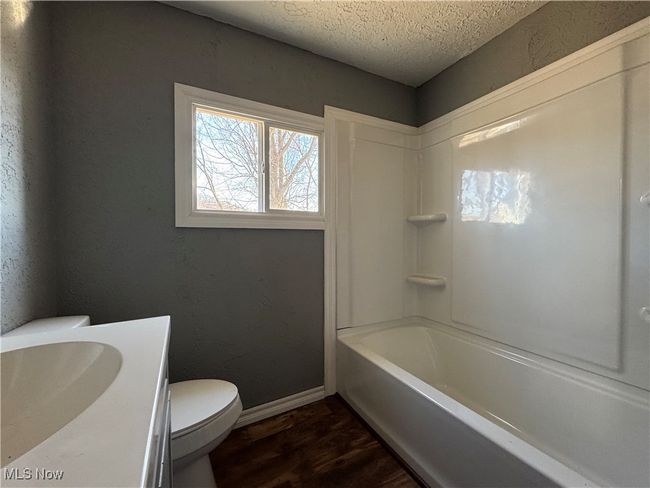 Full bathroom featuring toilet, vanity, a textured ceiling, wood finished floors, and baseboards | Image 12