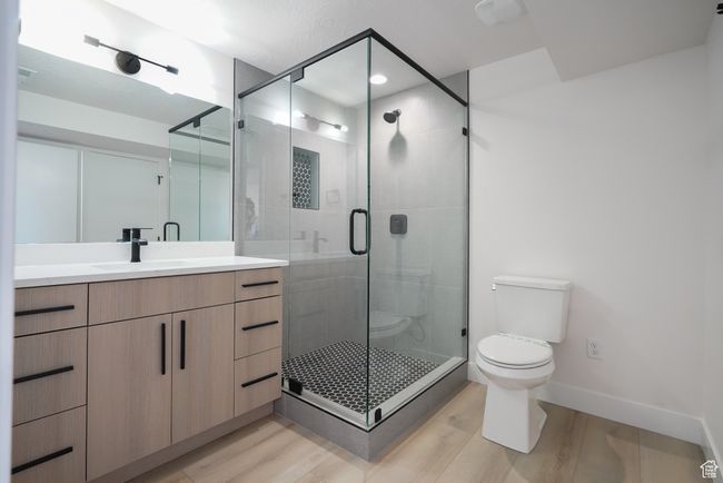 Bathroom featuring toilet, vanity, wood finished floors, a shower stall, and baseboards | Image 26