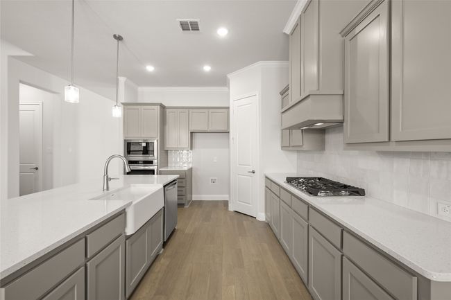 Kitchen with stainless steel appliances, a sink, gray cabinets, light wood-style flooring, and decorative backsplash | Image 8