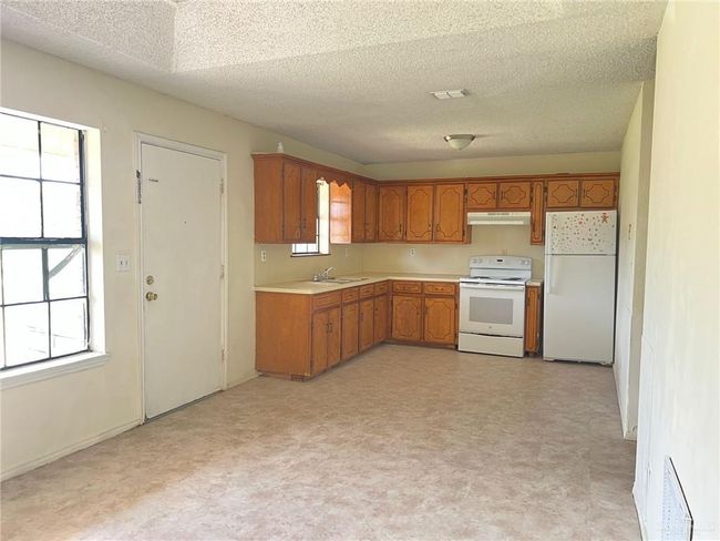 Kitchen with white appliances, under cabinet range hood, light flooring, light countertops, and brown cabinets | Image 4