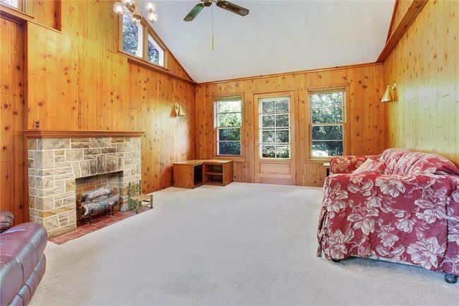 Carpeted living room with vaulted ceiling, wooden walls, healthy amount of natural light, ceiling fan, and a stone fireplace | Image 9