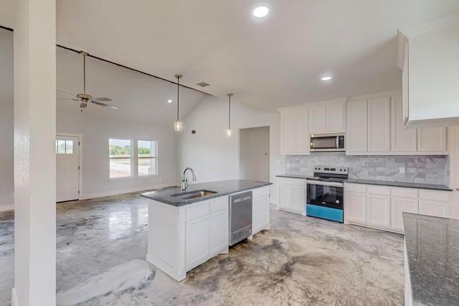 Kitchen with vaulted ceiling, decorative backsplash, stainless steel appliances, finished concrete floors, and a sink | Image 10