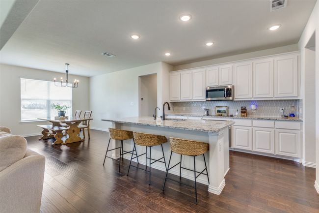 Kitchen featuring stainless steel microwave, decorative backsplash, a breakfast bar, a chandelier, and white cabinets | Image 6
