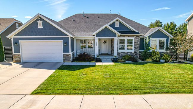 Craftsman-style home featuring stone siding, concrete driveway, an attached garage, a front lawn, and a shingled roof | Image 57