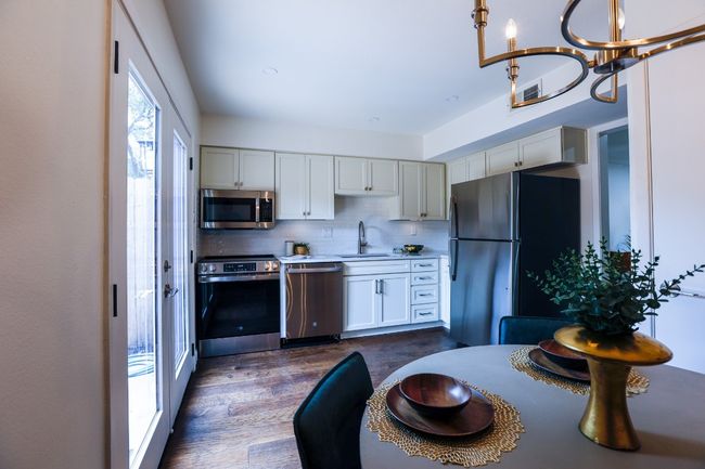 Kitchen featuring appliances stainless steel finishes, tasteful backsplash, light quartz countertops, dark engineered hardwood type flooring, and a chandelier. | Image 16