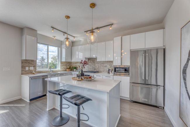 Kitchen featuring appliances with stainless steel finishes, light wood finished floors, white cabinetry, a kitchen bar, and backsplash | Image 11