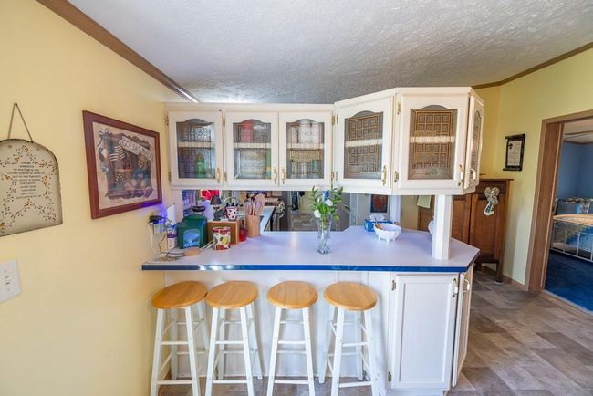 Kitchen with glass insert cabinets, a peninsula, ornamental molding, a textured ceiling, and a kitchen breakfast bar | Image 7