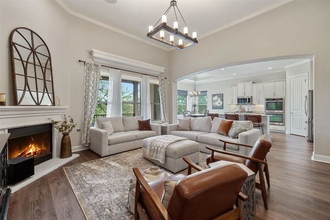 Living room featuring an inviting chandelier, arched walkways, crown molding, and a lit fireplace | Image 5