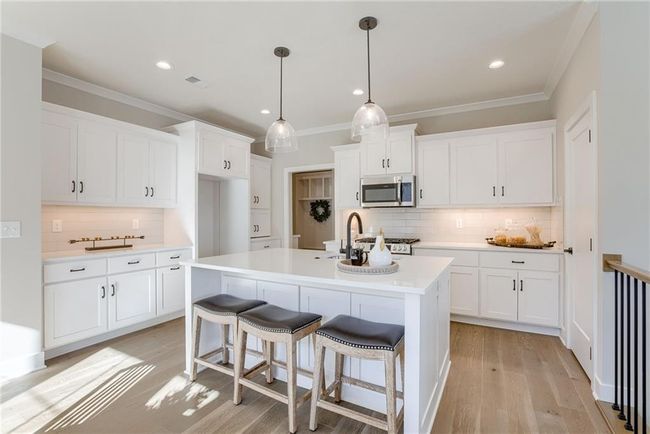 Kitchen with crown molding, white cabinets, stainless steel microwave, a sink, and decorative backsplash | Image 10