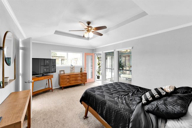 Carpeted bedroom featuring a raised ceiling, ornamental molding, a ceiling fan, and access to exterior | Image 22
