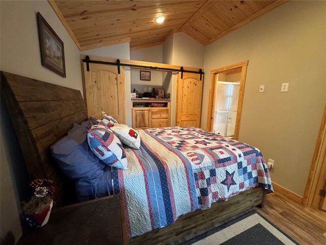 Bedroom with wooden ceiling, lofted ceiling, a barn door, crown molding, and wood finished floors | Image 34