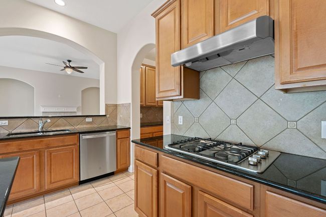 Kitchen with a sink, decorative backsplash, under cabinet range hood, stainless steel appliances, and ceiling fan | Image 10