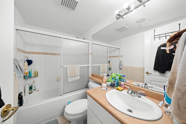 Bathroom with combined bath / shower with glass door, visible vents, toilet, and vanity | Image 10