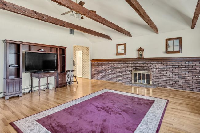 Living area with lofted ceiling with beams, wood finished floors, ceiling fan, and a fireplace | Image 11