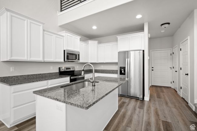 Kitchen with stainless steel appliances, wood finished floors, white cabinets, dark stone counters, and recessed lighting | Image 9