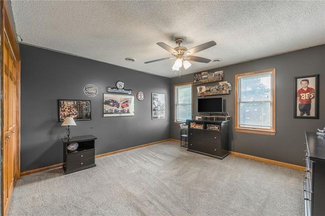 Carpeted home office featuring a textured ceiling, visible vents, baseboards, and a ceiling fan | Image 54