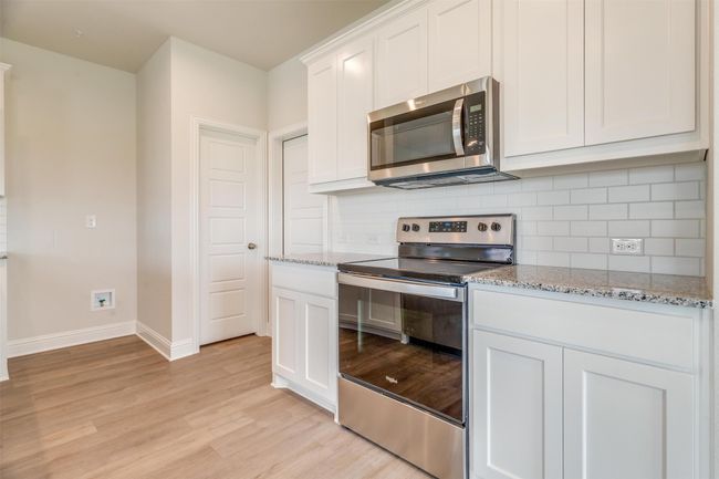 Kitchen with light hardwood / wood-style flooring, appliances with stainless steel finishes, white cabinetry, backsplash, and light stone countertops | Image 13