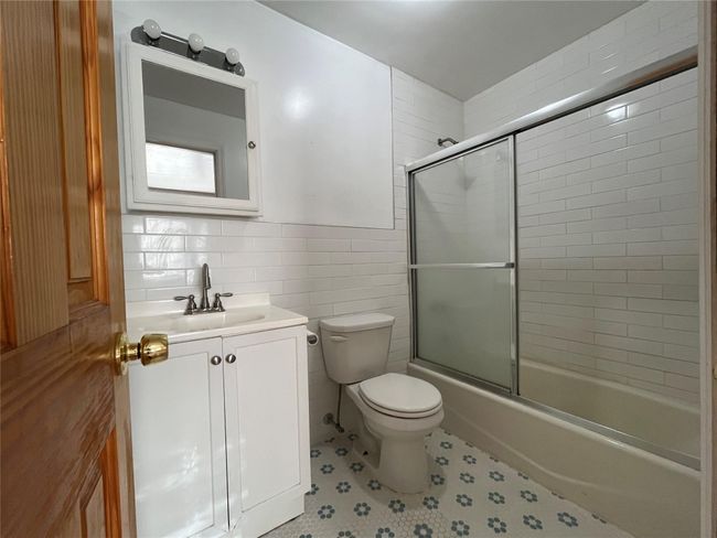 Bathroom featuring bath / shower combo with glass door, vanity, tile walls, and toilet | Image 13