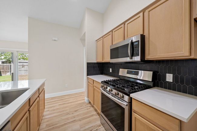 Kitchen with stainless steel appliances, light brown cabinets, light wood-style flooring, decorative backsplash, and light countertops | Image 13