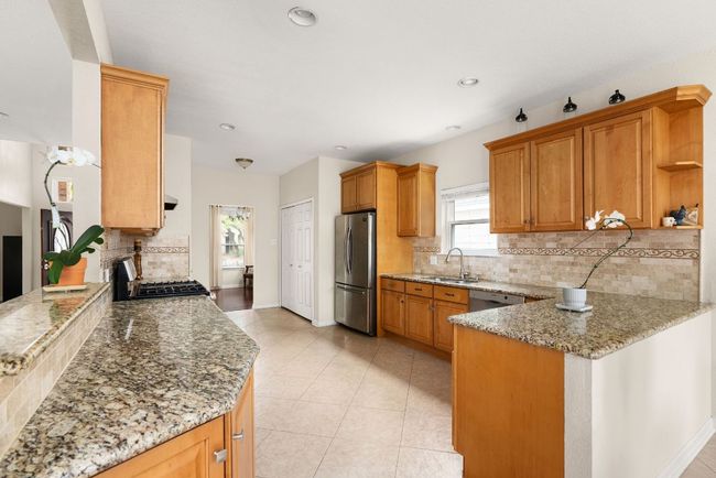 Kitchen featuring light tile patterned floors, baseboards, a peninsula, light stone countertops, and stainless steel appliances | Image 8