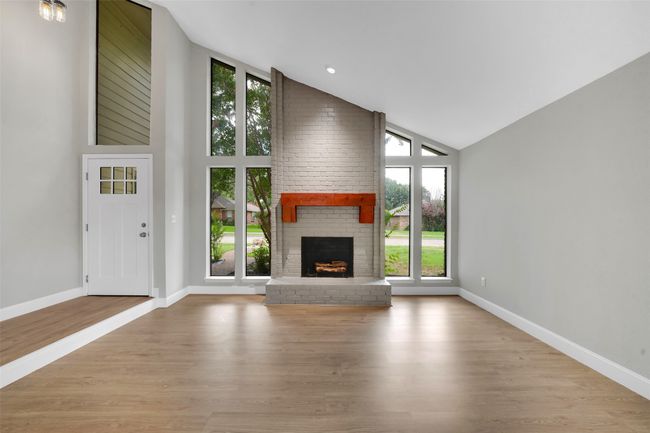 Unfurnished living room with plenty of natural light, a brick fireplace, wood finished floors, and high vaulted ceiling | Image 5