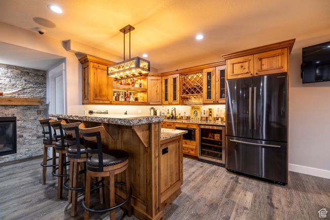 Indoor wet bar with freestanding refrigerator, wine cooler, dark wood-style flooring, hanging light fixtures, and black microwave | Image 39