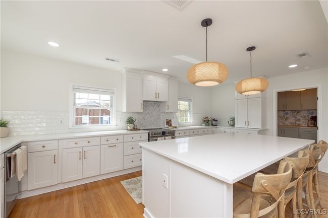 Kitchen featuring light countertops, light wood-type flooring, stainless steel appliances, a kitchen island, and white cabinets | Image 10