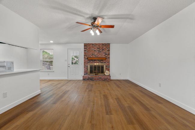 Unfurnished living room with a ceiling fan, wood finished floors, a textured ceiling, and a brick fireplace | Image 11