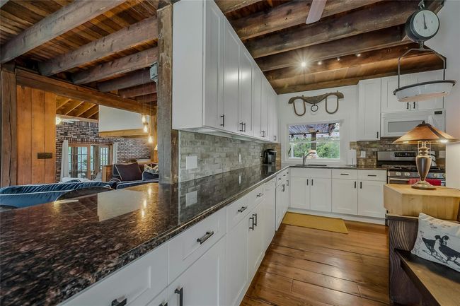 Kitchen featuring white microwave, wood ceiling with exposed beams, stainless steel range with gas cooktop, a sink, and light wood finished floors | Image 8