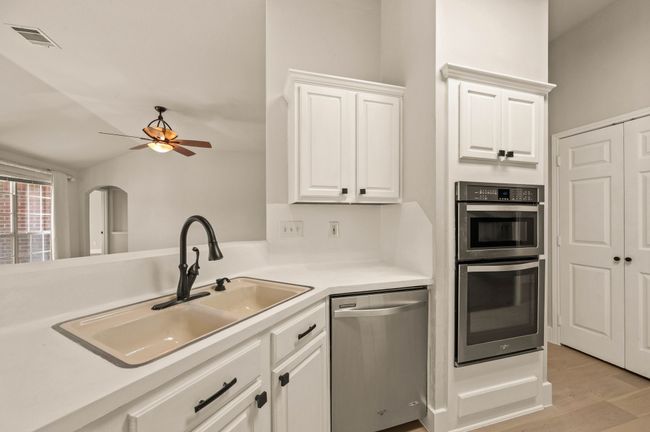 Kitchen with visible vents, ceiling fan, stainless steel appliances, white cabinetry, and a sink | Image 15