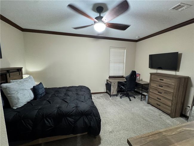 Bedroom with crown molding, light carpet, a textured ceiling, a ceiling fan, and an office area | Image 19