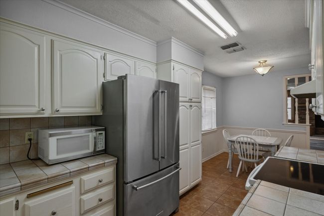 Kitchen with white appliances, tile countertops, backsplash, a textured ceiling, and tile patterned floors | Image 23