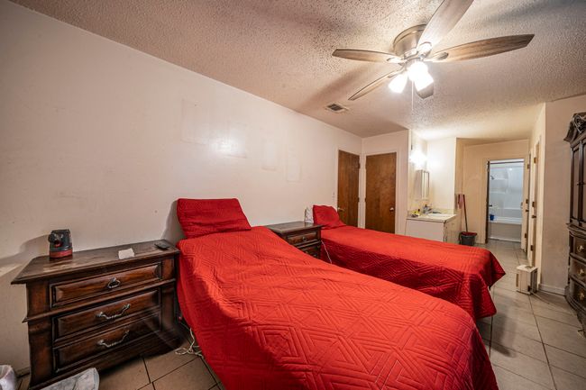 Tiled bedroom featuring a textured ceiling, connected bathroom, and ceiling fan | Image 16