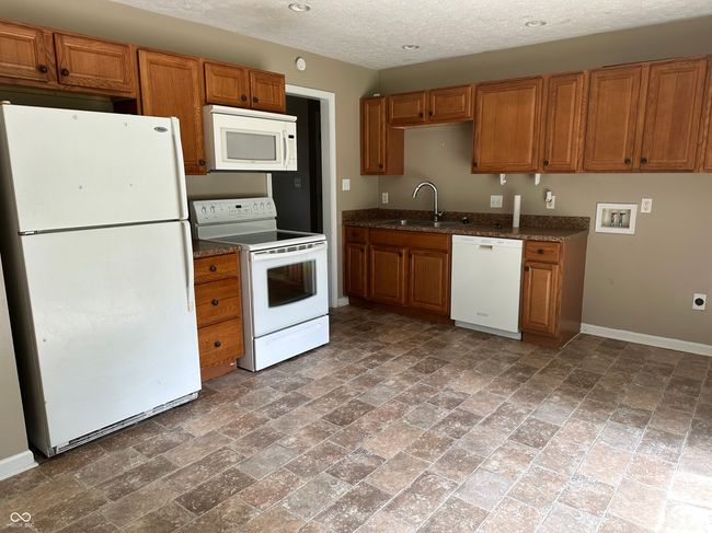 kitchen with white appliances, brown cabinets, dark stone counters, and a textured ceiling | Image 10