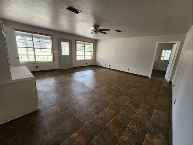 Unfurnished living room featuring a ceiling fan, stone finish floors, and a textured ceiling | Image 6