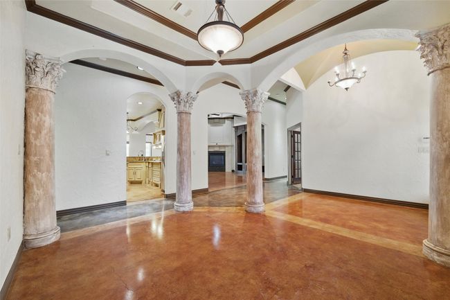 Unfurnished room featuring finished concrete flooring, ornate columns, ornamental molding, a tray ceiling, and arched walkways | Image 10