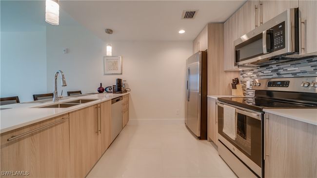 Kitchen featuring hanging light fixtures, sink, light brown cabinetry, appliances with stainless steel finishes, and tasteful backsplash | Image 14