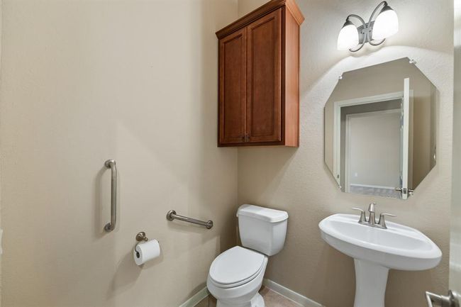 At the left of entryway there is a convenient half bath. The half bath features tile floors, a pedestal sink, and built-in wooden cabinets for storage. | Image 14