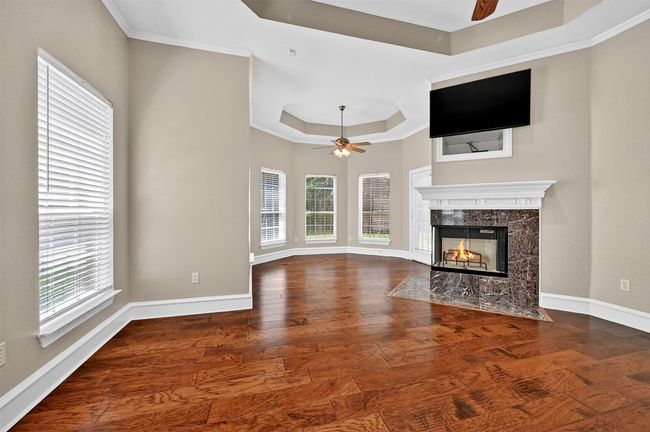 Unfurnished living room featuring a ceiling fan, a tray ceiling, healthy amount of natural light, a fireplace, and crown molding | Image 20