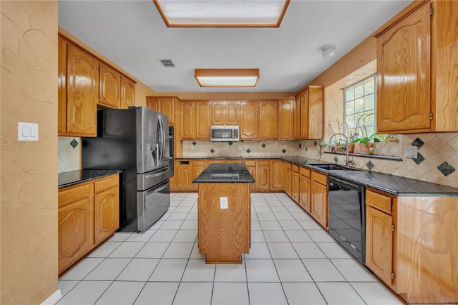 Kitchen featuring a center island, stainless steel appliances, tasteful backsplash, light tile patterned flooring, and brown cabinets | Image 5
