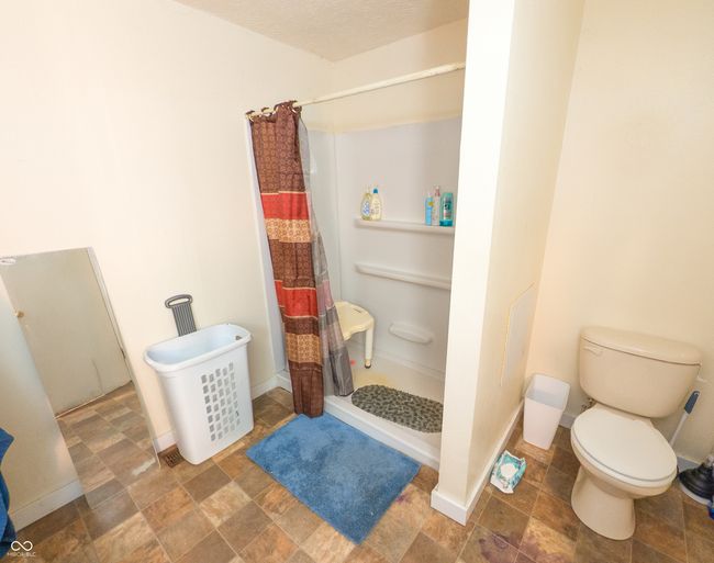 full bath featuring a shower with curtain, toilet, stone finish floors, and baseboards | Image 6