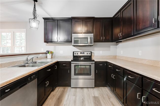 Kitchen with stainless steel appliances, a sink, light countertops, decorative light fixtures, and light wood-style floors | Image 8