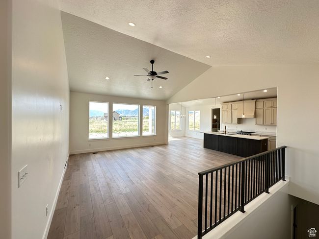 Unfurnished living room with a textured ceiling, vaulted ceiling, a ceiling fan, light wood-type flooring, and recessed lighting | Image 5